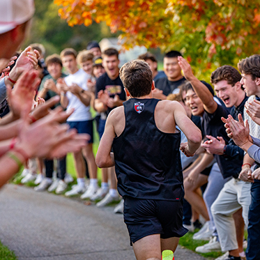 An athlete running along side a group of students cheering. Links to Gifts of Real Estate